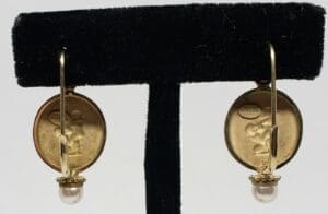 Gold earrings with pearls on black stand.
