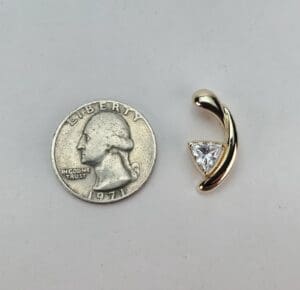 Gold pendant with diamond beside a quarter.