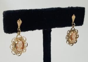 Gold cameo earrings on display stand.