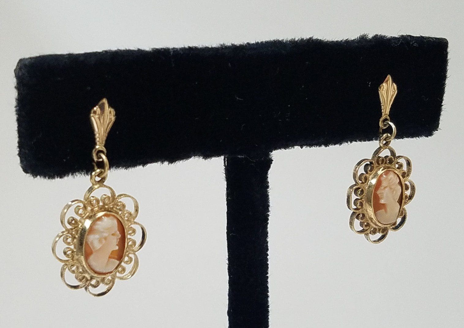 Gold cameo earrings on display stand.