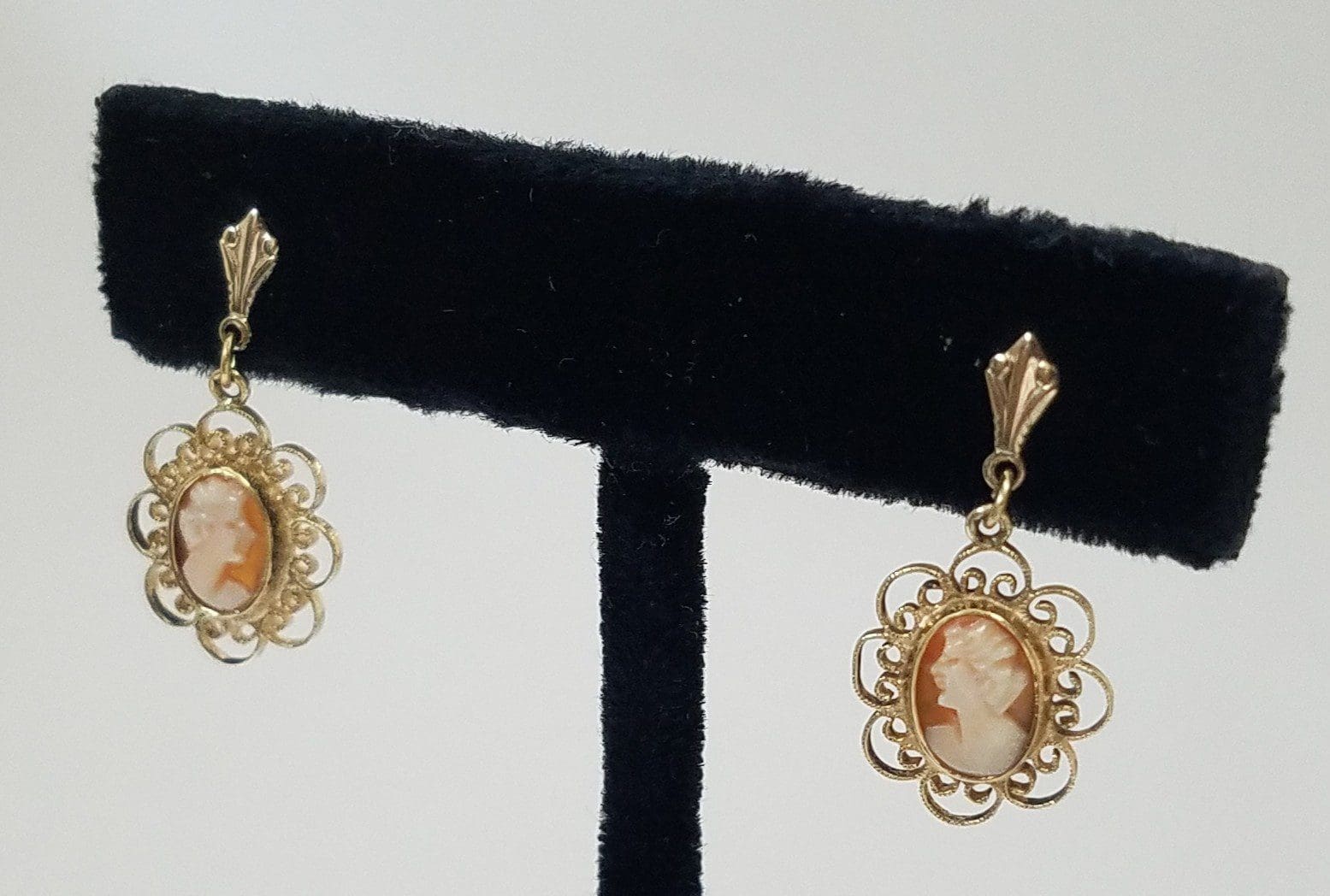 Vintage cameo earrings on black display stand.