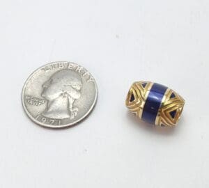 Gold and blue bead beside a quarter.