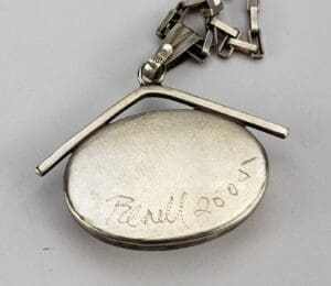 Silver pendant with chain and engraved text.