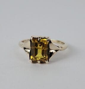 Gold ring with rectangular yellow gemstone.