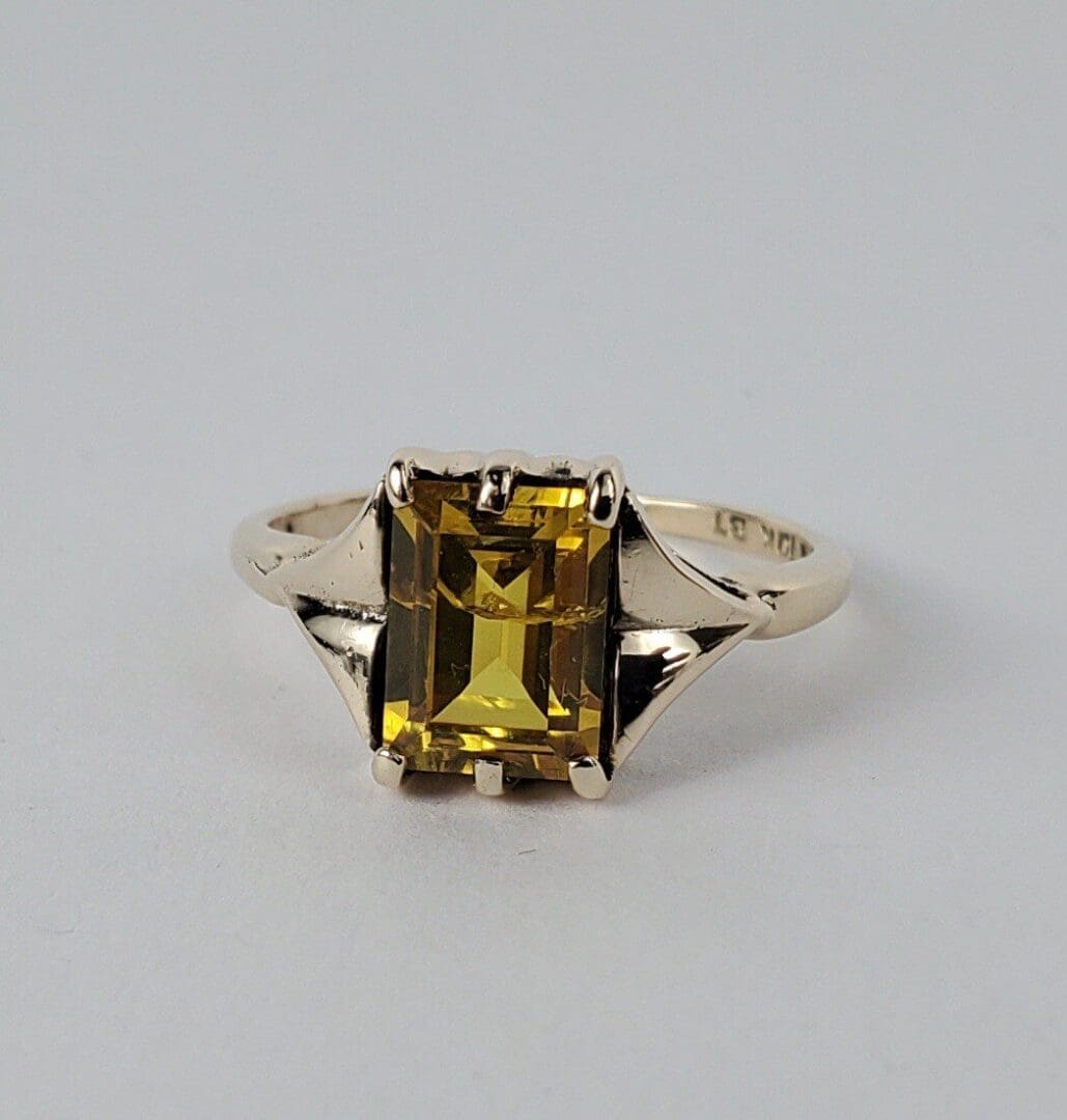 Gold ring with rectangular yellow gemstone.
