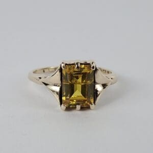 Gold ring with yellow rectangular gemstone.