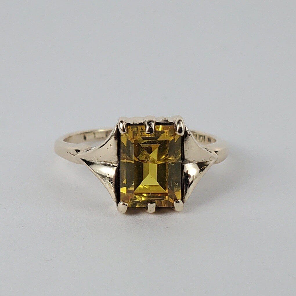 Gold ring with yellow rectangular gemstone.
