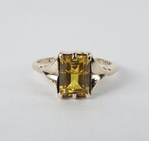 Gold ring with yellow rectangular gemstone.