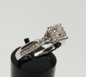 Diamond engagement ring on black stand.