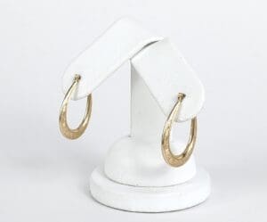 Gold hoop earrings on white display stand.
