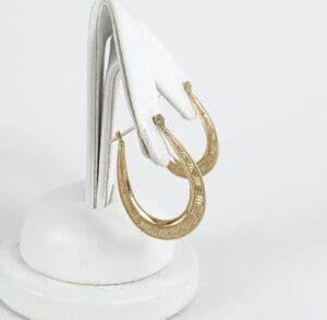 Gold hoop earrings on white display stand.