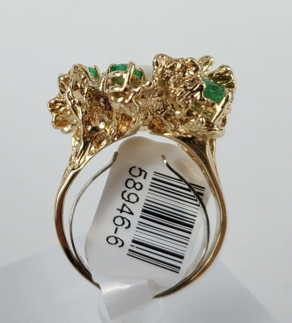 Gold ring with green gemstones and tag.