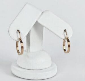 Gold hoop earrings on white display stand.