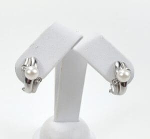Silver earrings with pearls on display stand.