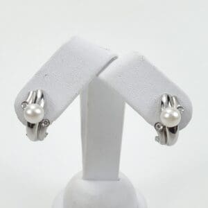 Silver and pearl earrings on white stand.