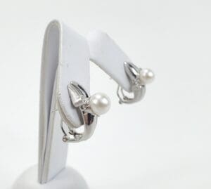 Silver earrings with pearls on display stand.