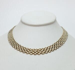 Gold choker necklace on white display stand.
