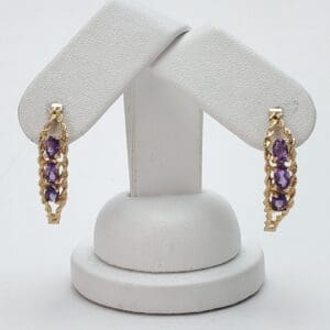 Gold earrings with purple gemstones on display.