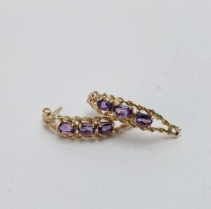 Gold earrings with purple gemstones on display.