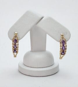 Gold earrings with purple gemstones on stand.
