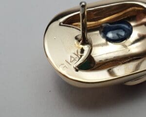 Gold earring with blue gemstone and stamp.
