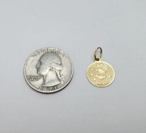 Quarter and small gold pendant side by side.