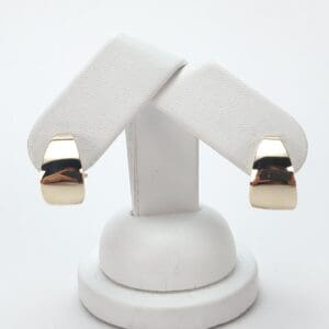 Gold earrings on a white display stand.
