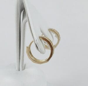 Gold hoop earrings on white display stand.