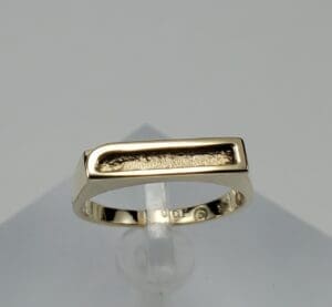 Gold ring with rectangular design on stand.