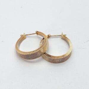Gold textured hoop earrings on white background.