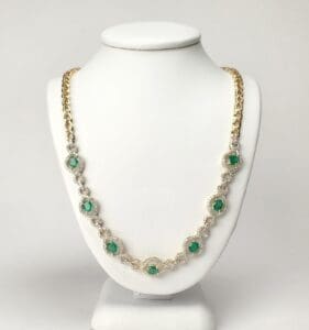 Gold necklace with green gemstones on display.