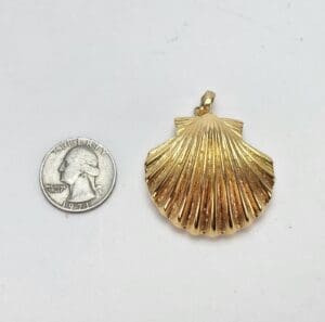 Gold shell pendant next to a quarter.