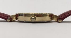Side view of gold watch with red strap.