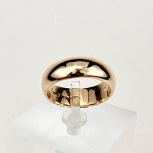 Gold ring displayed on a clear stand.