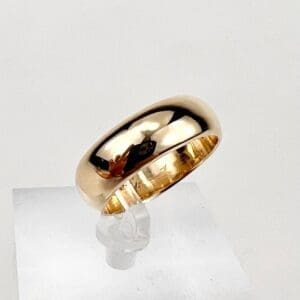 Gold band ring on white display stand.