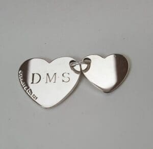 Two linked silver heart pendants, engraved.
