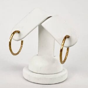 Gold hoop earrings on white display stand.