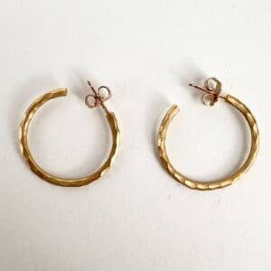 Gold textured hoop earrings on white background.