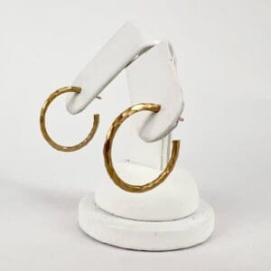 Gold textured hoop earrings on display stand.