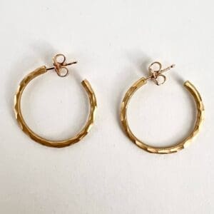 Gold textured hoop earrings on white background.