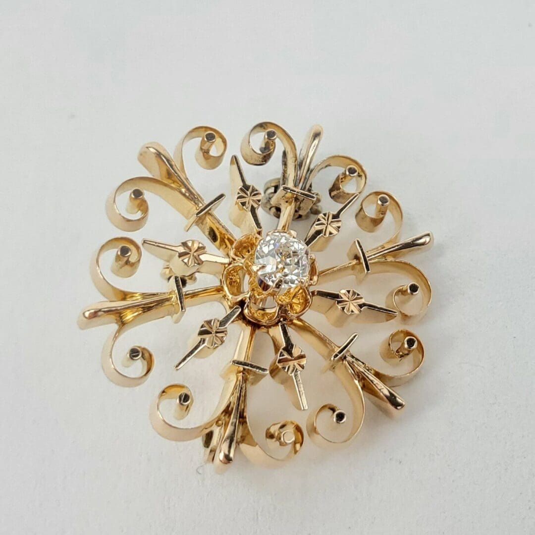 Gold brooch with intricate design and diamond.