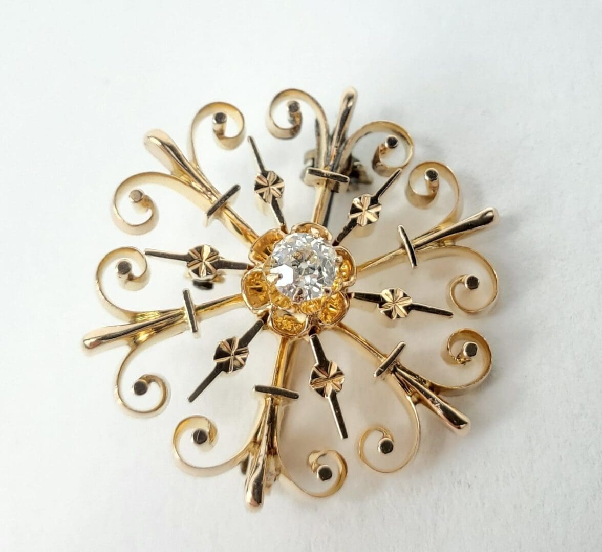 Ornate gold brooch with central diamond.