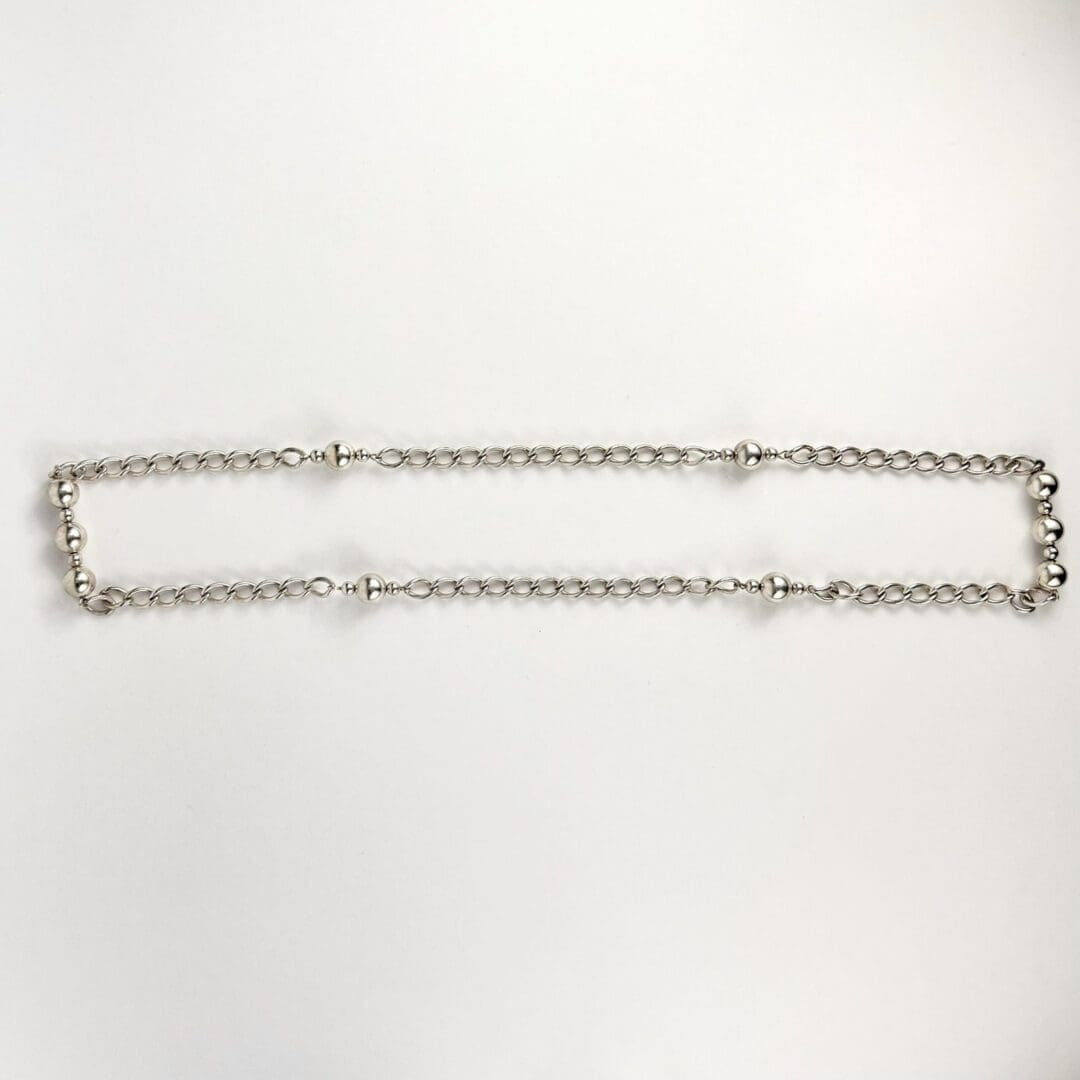 Silver chain with round beads on white.