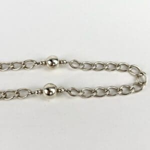 Silver chain with round beads on white.