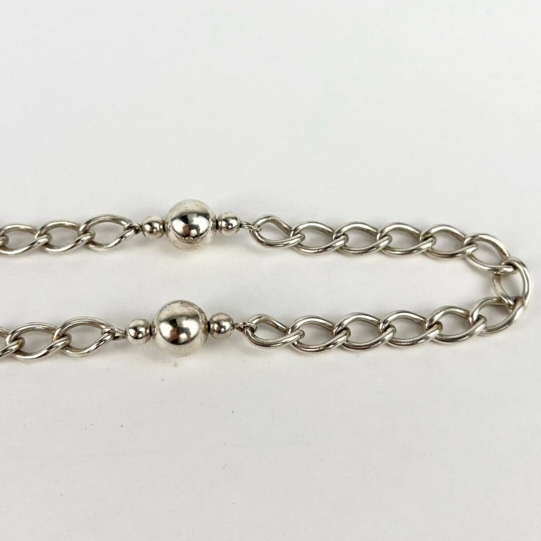 Silver chain with round beads on white.