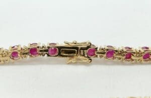 Gold bracelet with pink gemstones and clasp.