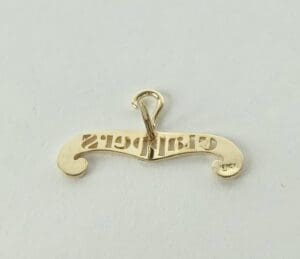 Gold pendant with engraved text facing backward.