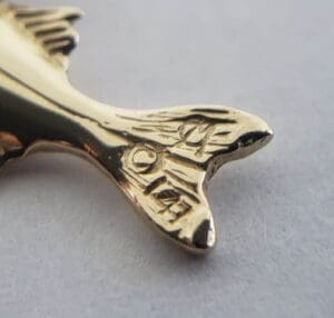 Gold fish-shaped pin on gray surface.