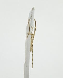Gold dangling earrings on white stand.