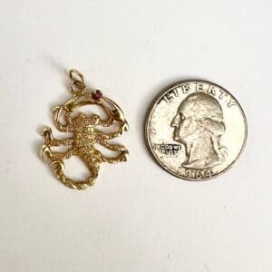 Gold scorpion pendant next to a quarter.